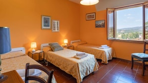 A hotel room with two single beds, a desk with a chair, a window with a view of the countryside, and a ceiling light. - Belvilla by OYO Selvatello Laura Trilo Cinque (Casole d'Elsa)