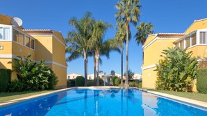 Ein Swimmingpool, umgeben von gelben Gebäuden mit Satellitenschüsseln, Palmen und üppiger Vegetation.