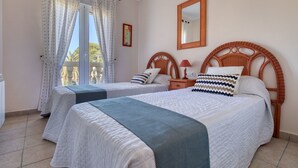 Ein Hotelzimmer mit zwei Betten, einem Balkon, einem Deckenventilator, einem Spiegel und einem Bild an der Wand.