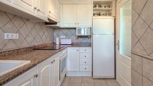 Eine kompakte Küche mit weißen Schränken, einer Mikrowelle, einem Kühlschrank und einer Arbeitsplatte aus Granit.