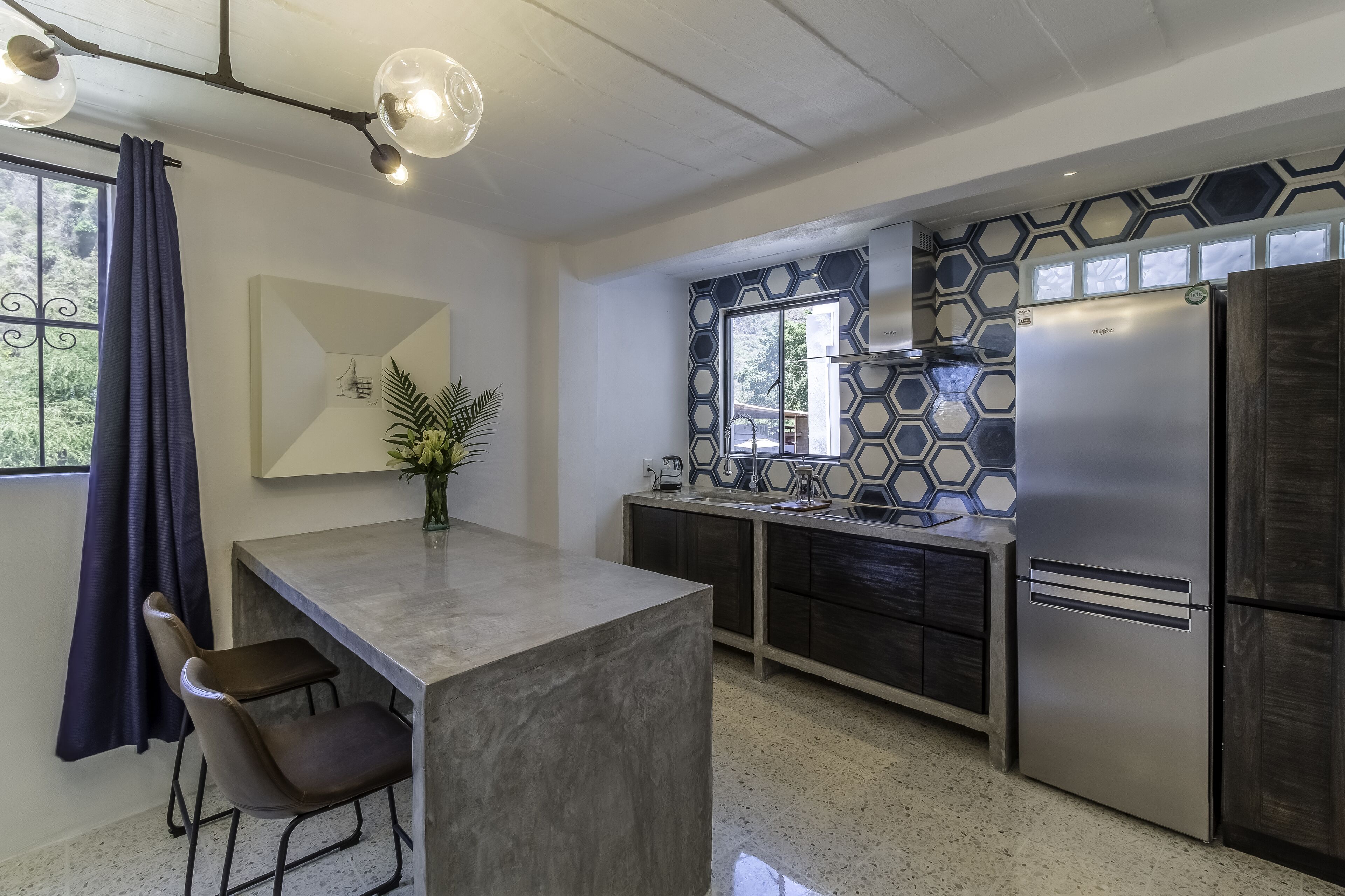 Cocina moderna con una isla central, electrodomésticos de acero inoxidable y un salpicadero de azulejos hexagonales.