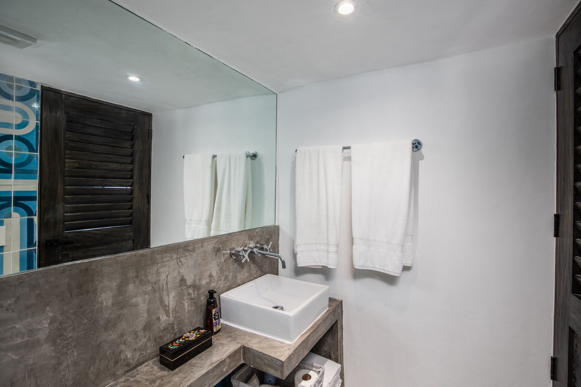 A modern bathroom with a large mirror, white sink, and two towels hanging on the wall.