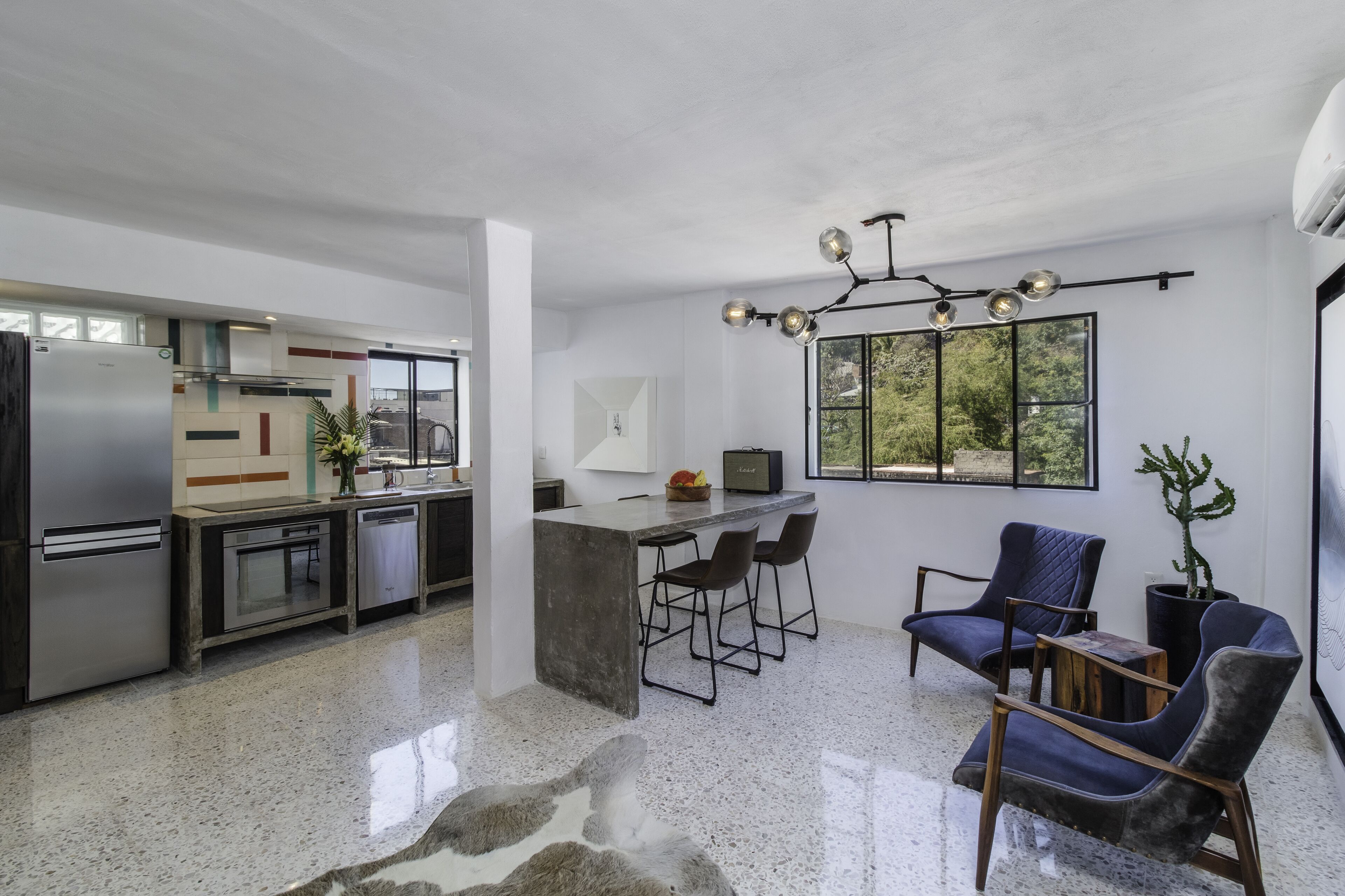 Una cocina moderna con una isla central, taburetes de bar y un comedor con un amplio ventanal.