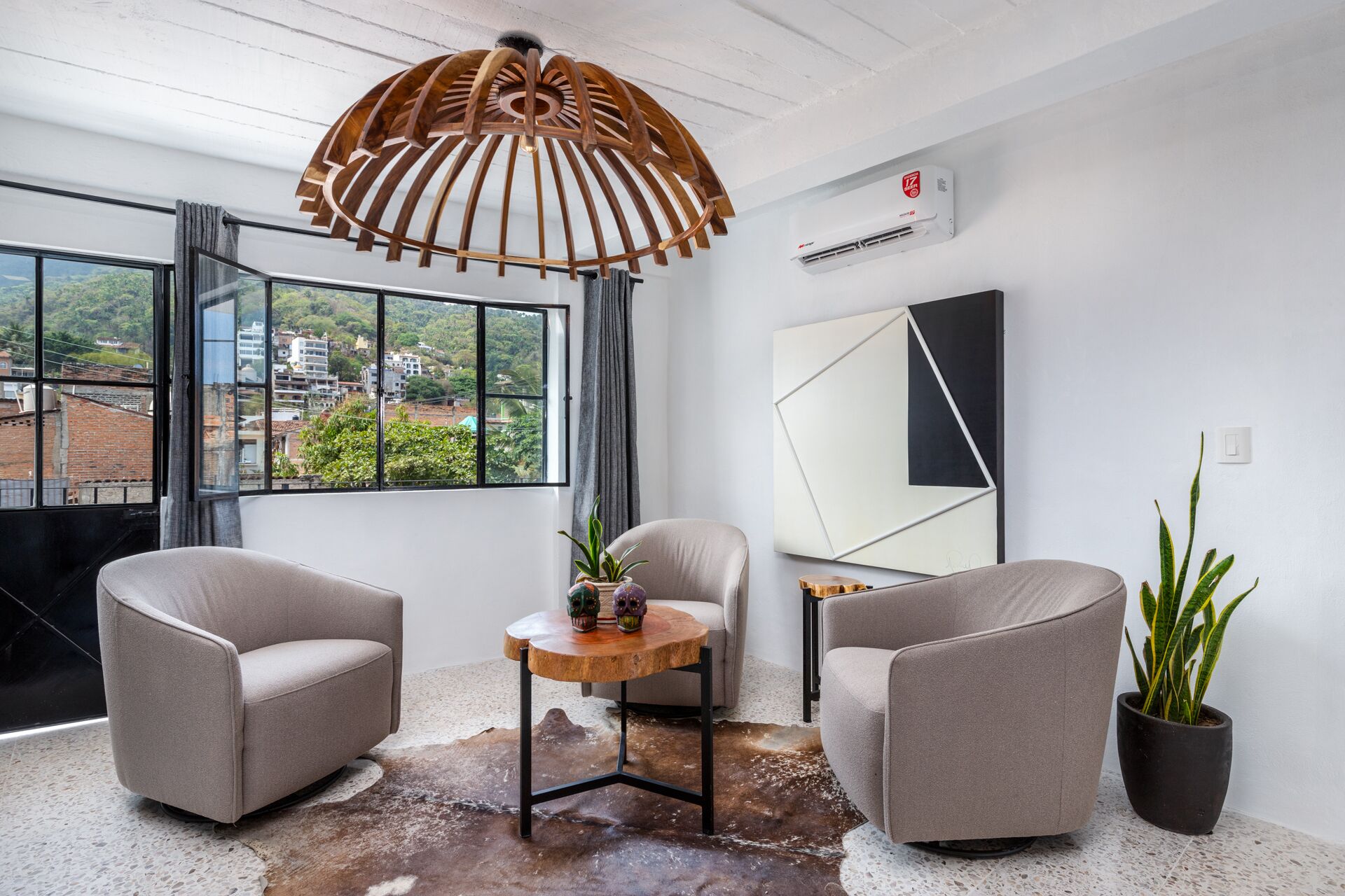 A modern room with two armchairs, a wooden coffee table, a large window with a view of buildings, and a ceiling light fixture.