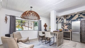 Een moderne keuken met een centraal eiland, een eethoek met stoelen, een groot raam met gordijnen en een plafond met zichtbare balken.