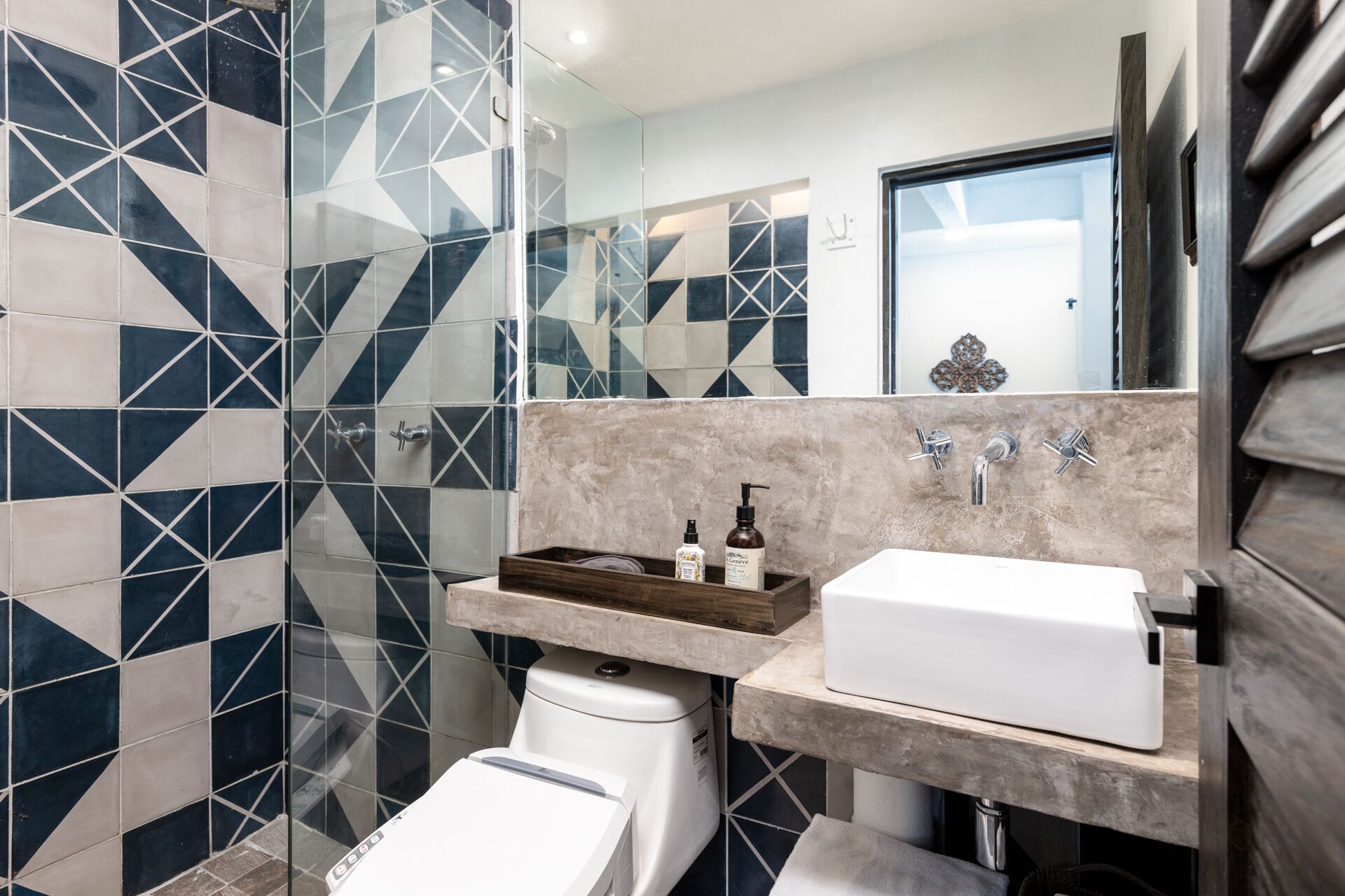 Un baño moderno con un salpicadero de azulejos geométricos, un lavabo blanco y un inodoro.