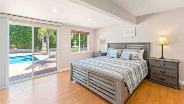 Une chambre à coucher avec un lit, des tables de chevet, une lampe et une vue sur une piscine.