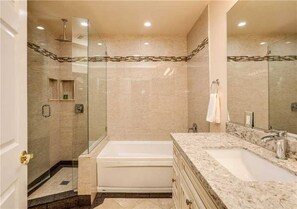 A modern bathroom with a glass-enclosed shower, a freestanding bathtub, and a marble vanity with a sink.