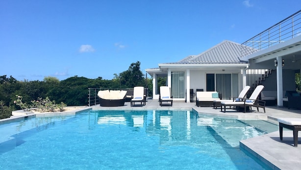 Un espace piscine moderne avec des chaises longues et un coin salon abrité.