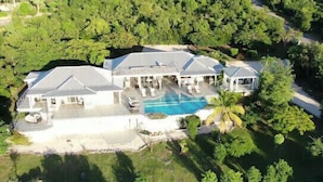Une grande maison avec une piscine, entourée d’une végétation luxuriante et de palmiers.