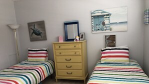 A bedroom with two single beds, a dresser, a lamp, and a mirror. - On top of the world condo  (Clearwater)