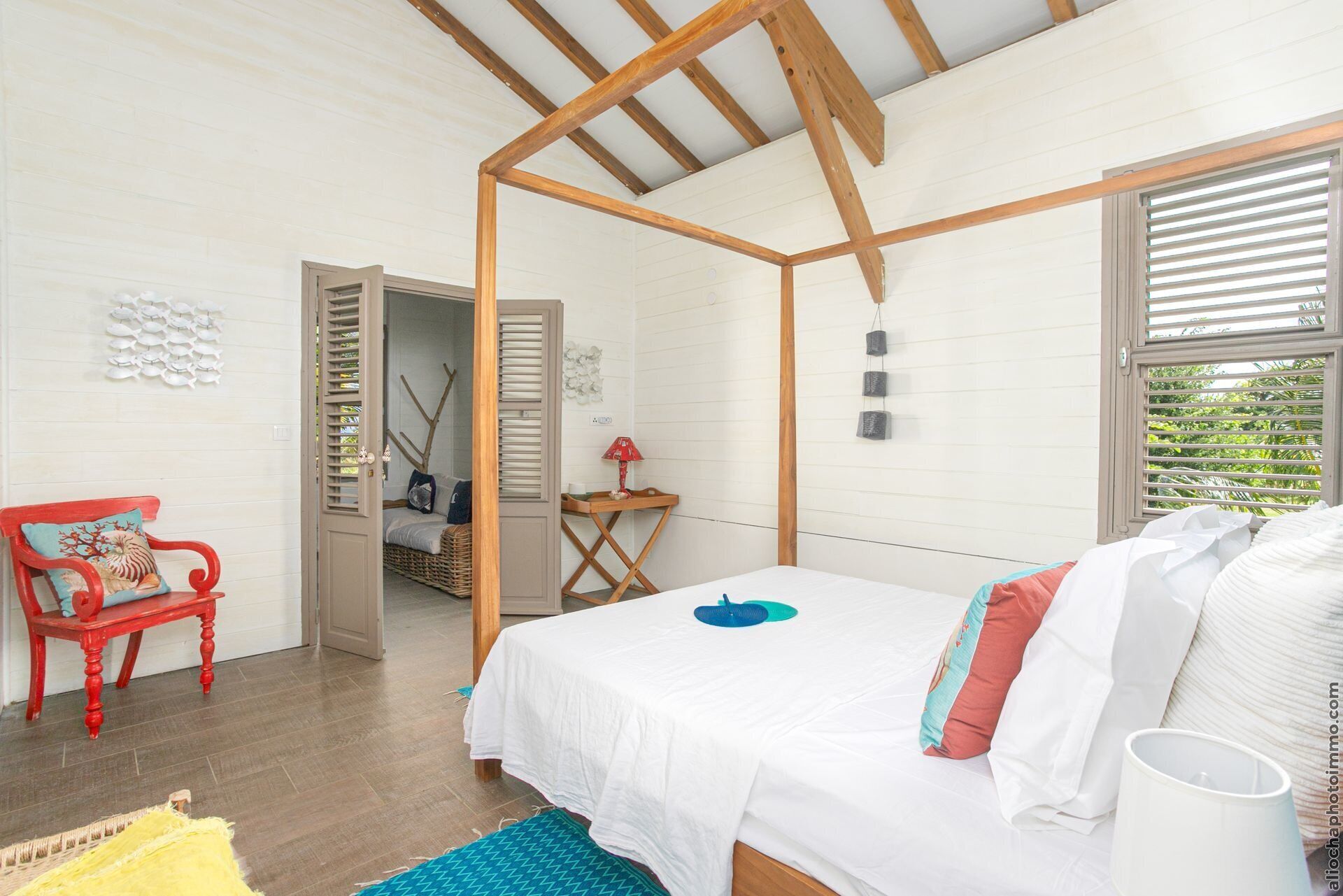 Ein Schlafzimmer mit Holzboden, einem Bett mit weißer Bettwäsche, einem roten Sessel und einem kleinen Tisch mit einer Lampe.