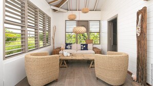 A cozy room with a wooden ceiling, wicker furniture, and a view of greenery outside. - LAGON BLANC (LE VAUCLIN)