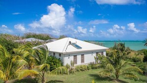 A white house with a flat roof, surrounded by lush greenery and a clear blue sky. - LAGON BLANC (LE VAUCLIN)