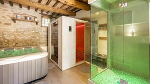 Una stanza spa con parete in pietra, travi in legno a soffitto, cabina doccia in vetro e vasca da bagno in legno.