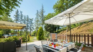 Patio esterno con tavolo apparecchiato per mangiare, circondato da sedie e un grande ombrellone.