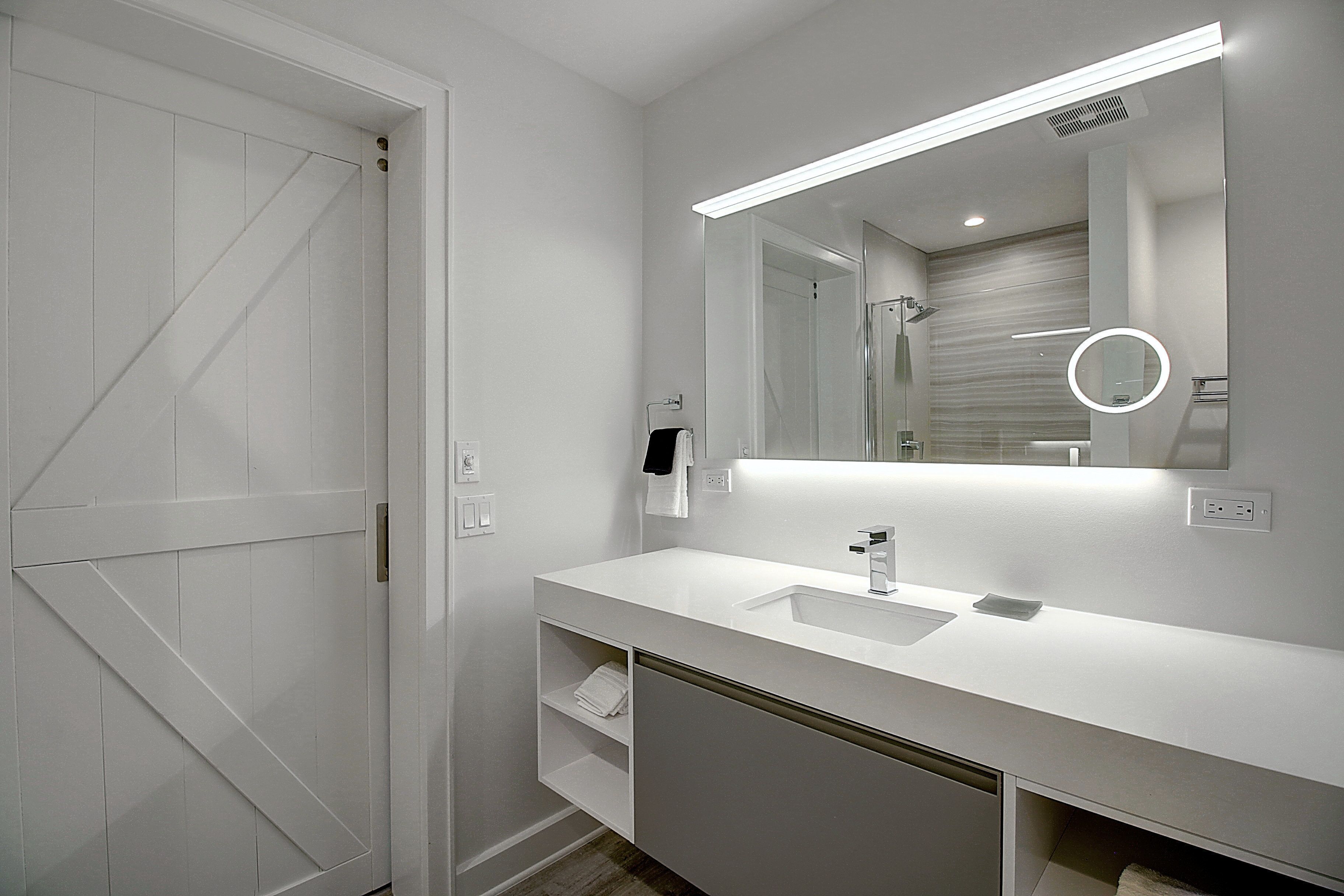 A modern bathroom with a white vanity, a large mirror, and a shower area.