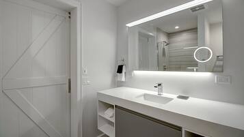 A modern bathroom with a white vanity, a large mirror, and a shower area.