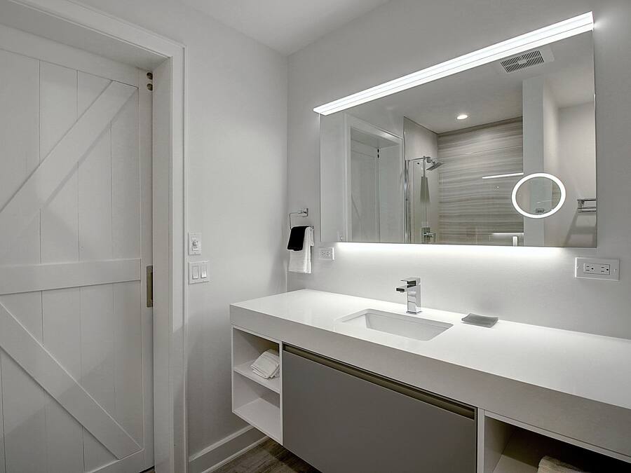 A modern bathroom with a white vanity, a large mirror, and a shower area.