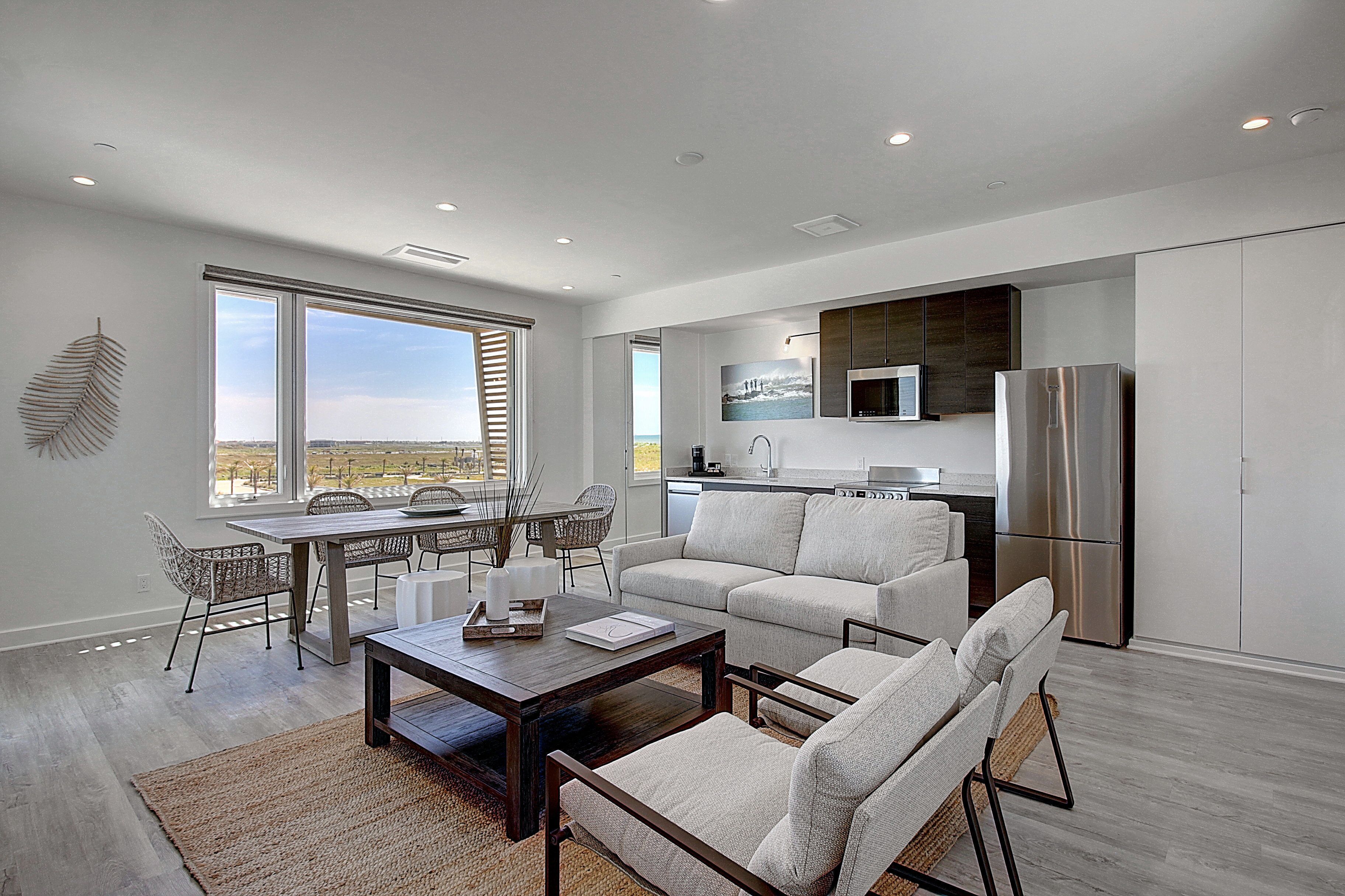 A modern living room with a dining area, a kitchen, and large windows offering a view.