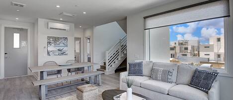 A modern living room with a sofa, coffee table, and a dining area with a bench and chairs.