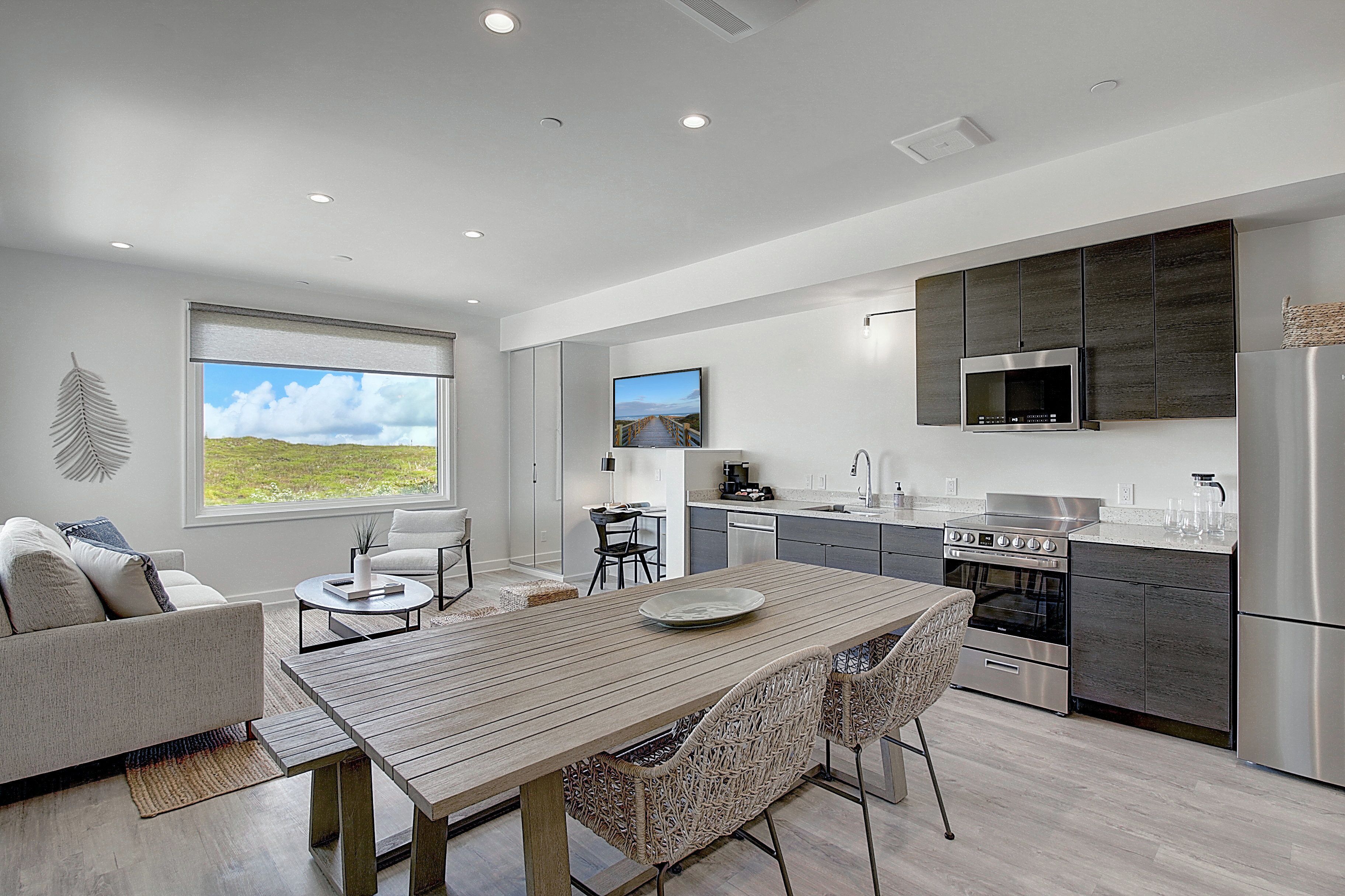 A modern kitchen with a dining area, featuring a large window, stainless steel appliances, and a view of the outdoors.