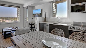 A modern kitchen with a large window, a dining area with a wooden table, wicker chairs, and a built-in oven. - Lively Beach (Corpus Christi)