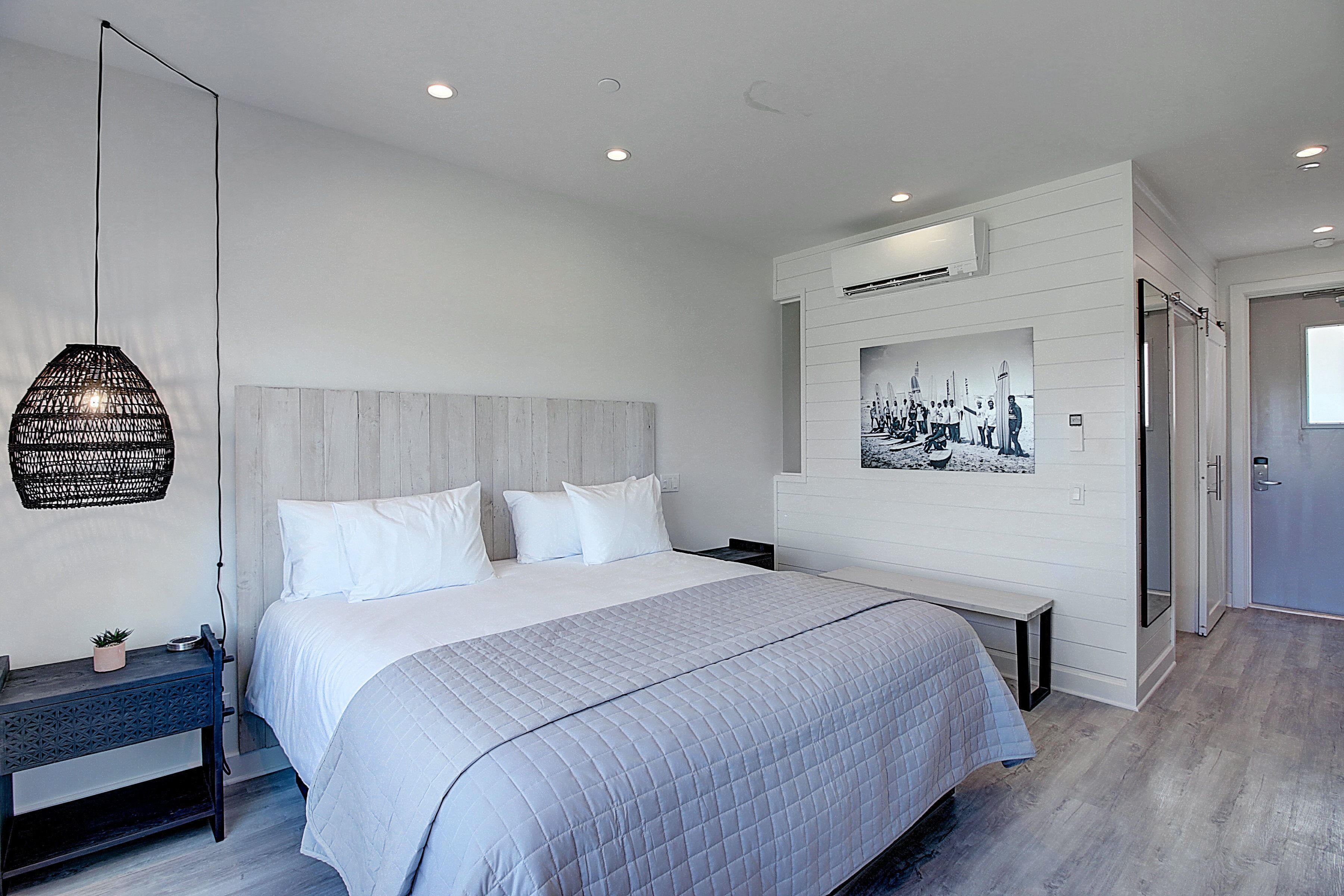 A modern bedroom with a large bed, a bedside table, a hanging light fixture, and a wall-mounted air conditioner.