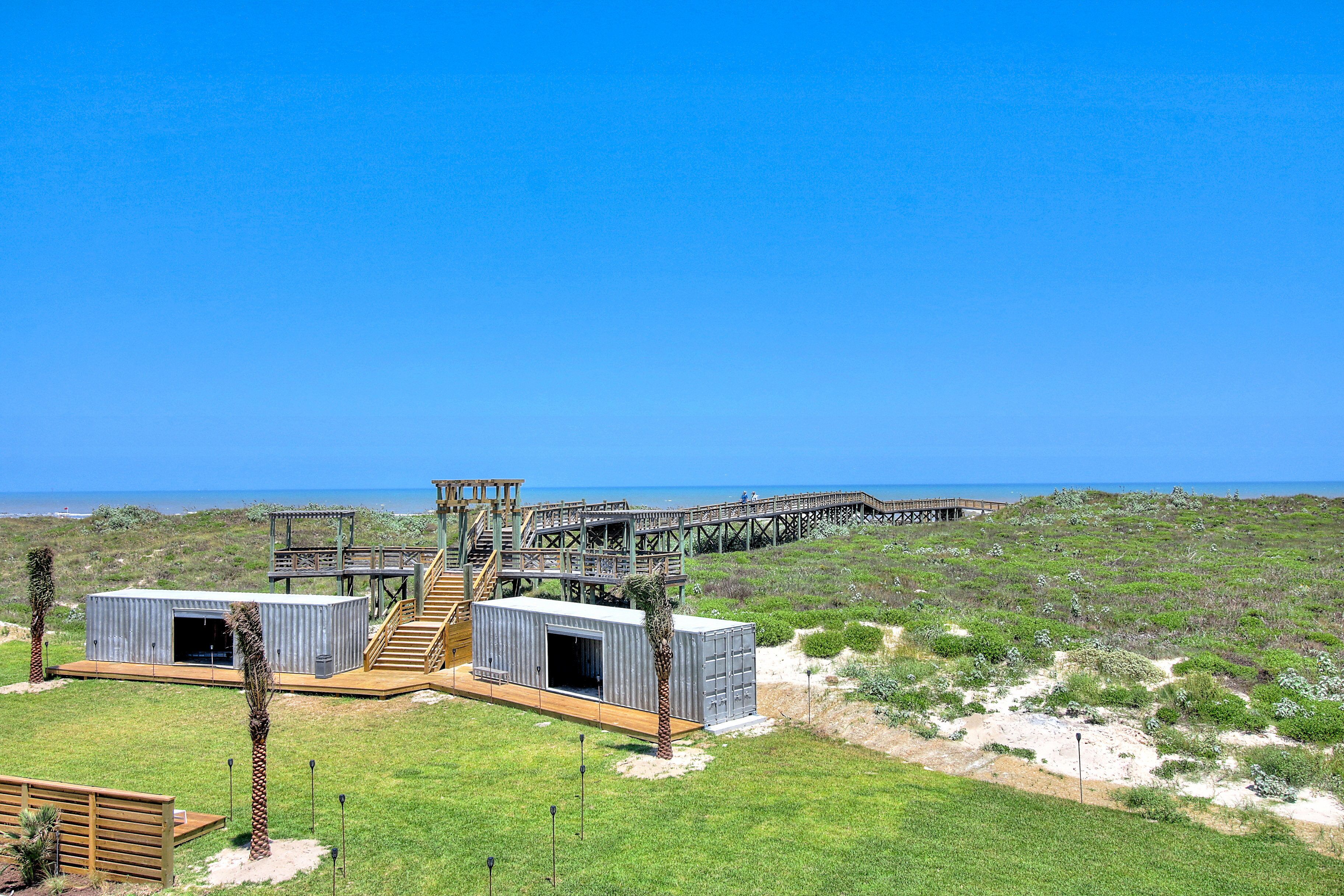 A coastal property with a wooden deck, two metal cabins, and a pier extending into the sea.