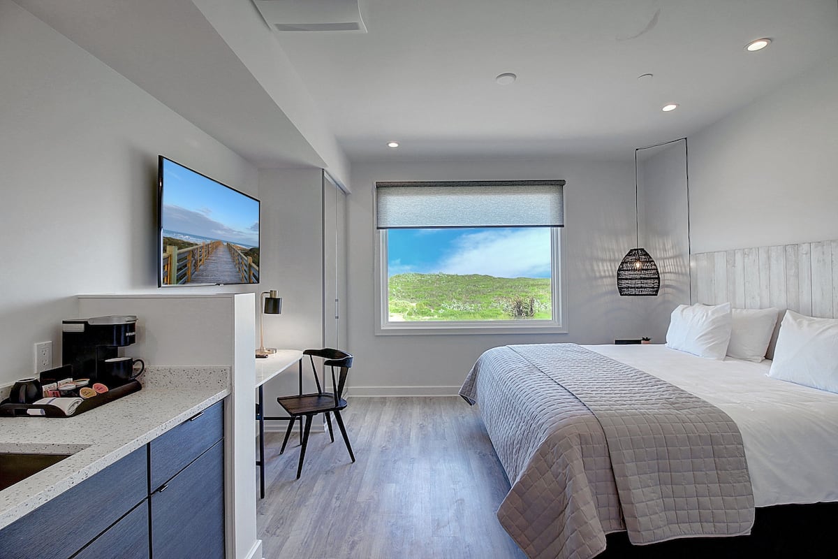 Un dormitorio moderno con una cama grande, un escritorio con silla, una ventana con vistas a zonas verdes y un televisor de pantalla plana montado en la pared.