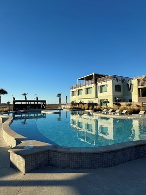 Un hôtel moderne doté d’une piscine, de chaises longues et d’une terrasse couverte.