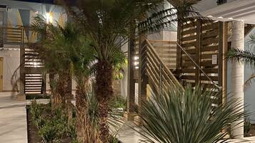 A building with a wooden staircase and a garden with palm trees.