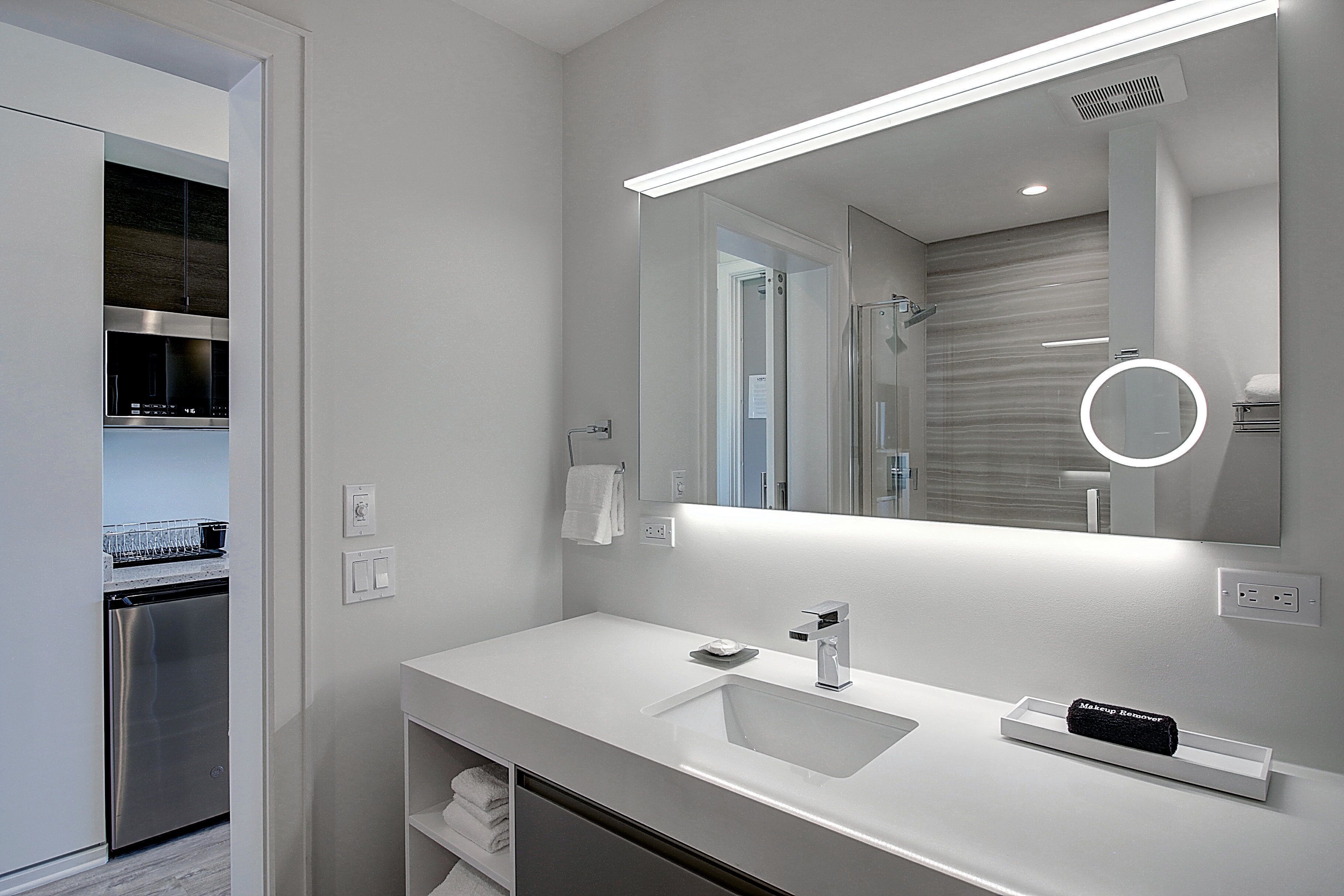 A modern bathroom with a white sink, a mirror with integrated lighting, and a built-in shower.
