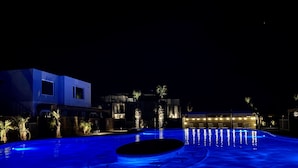 A swimming pool with a blue-lit edge, surrounded by modern buildings and palm trees. - Lively Beach (Corpus Christi)