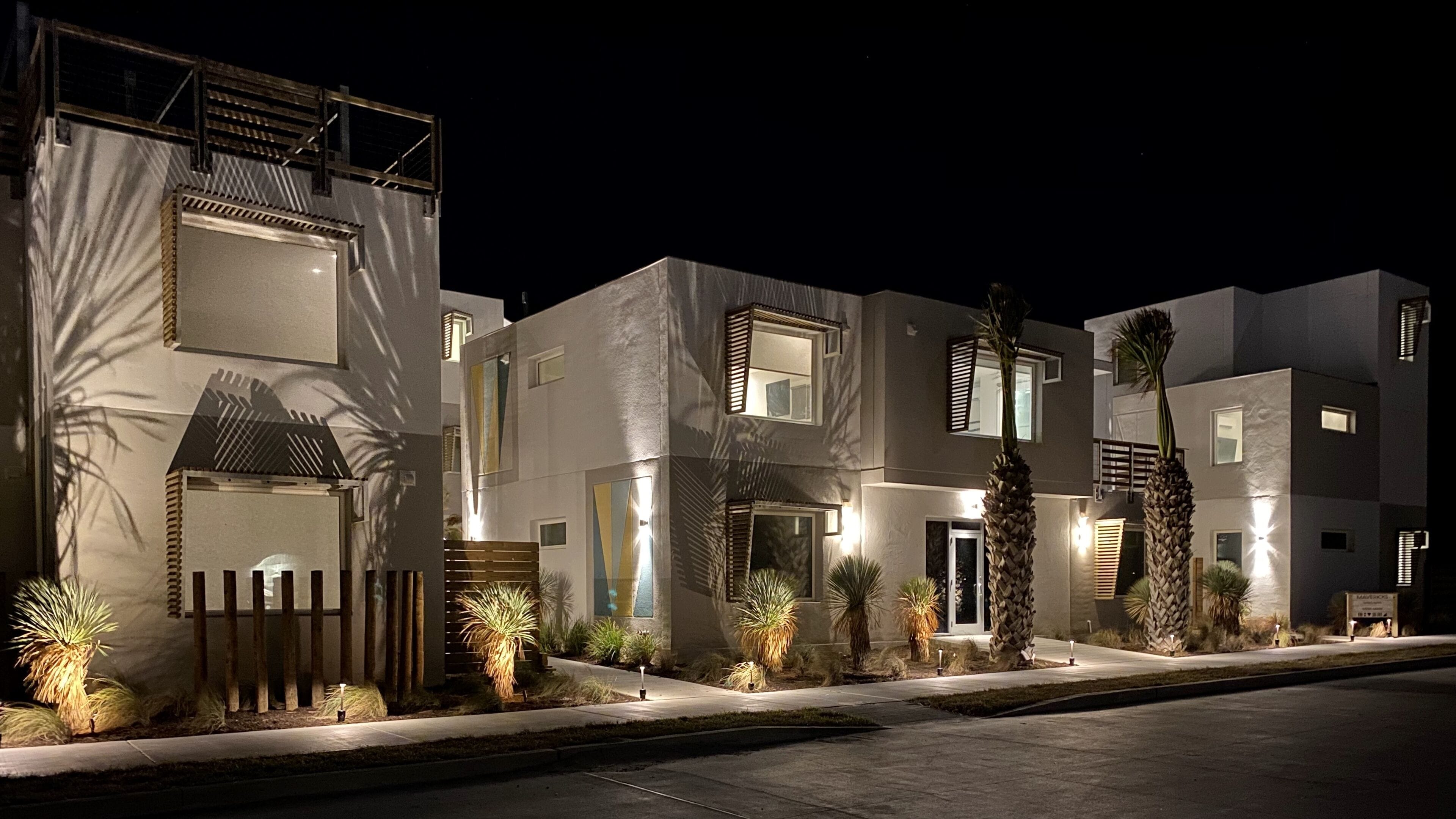 A modern multi-story residential building with a well-lit entrance and a gated driveway.