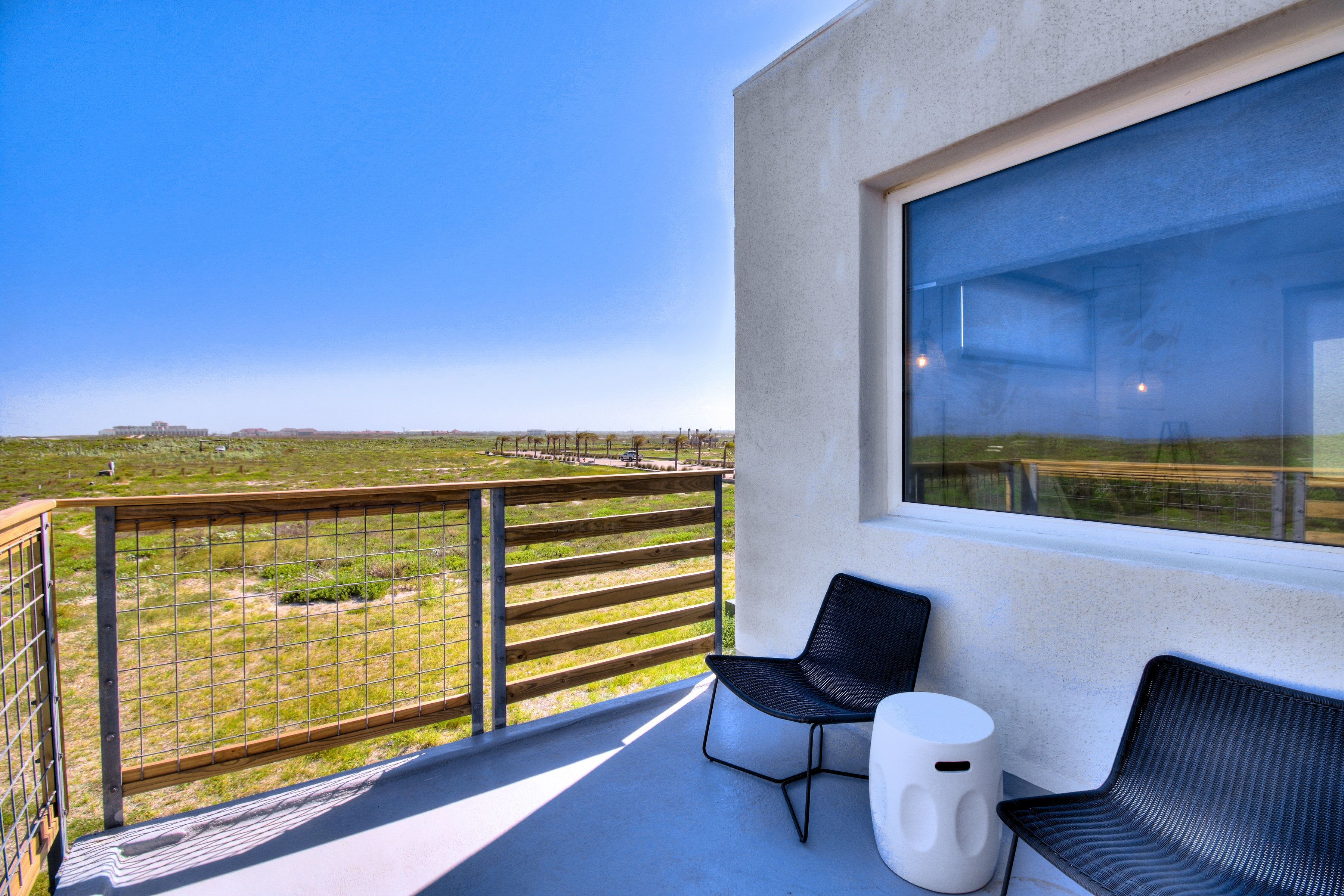 A balcony with a view of a vineyard, a large window, and two black chairs with a small white table.