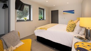 A modern bedroom with a bed, a bedside table with a lamp, a chair, and two windows with plants. - The Mount,  2 ensuite double rooms by The Royal William Yard (Plymouth)
