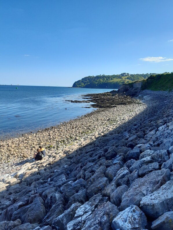 A rocky beach with a clear view of the sea and a distant hill.