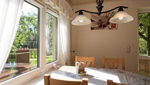 A dining area with a table set for two, a chandelier, and a view of a garden through large windows. - Apartment in Saxony With Terrace (Crottendorf)