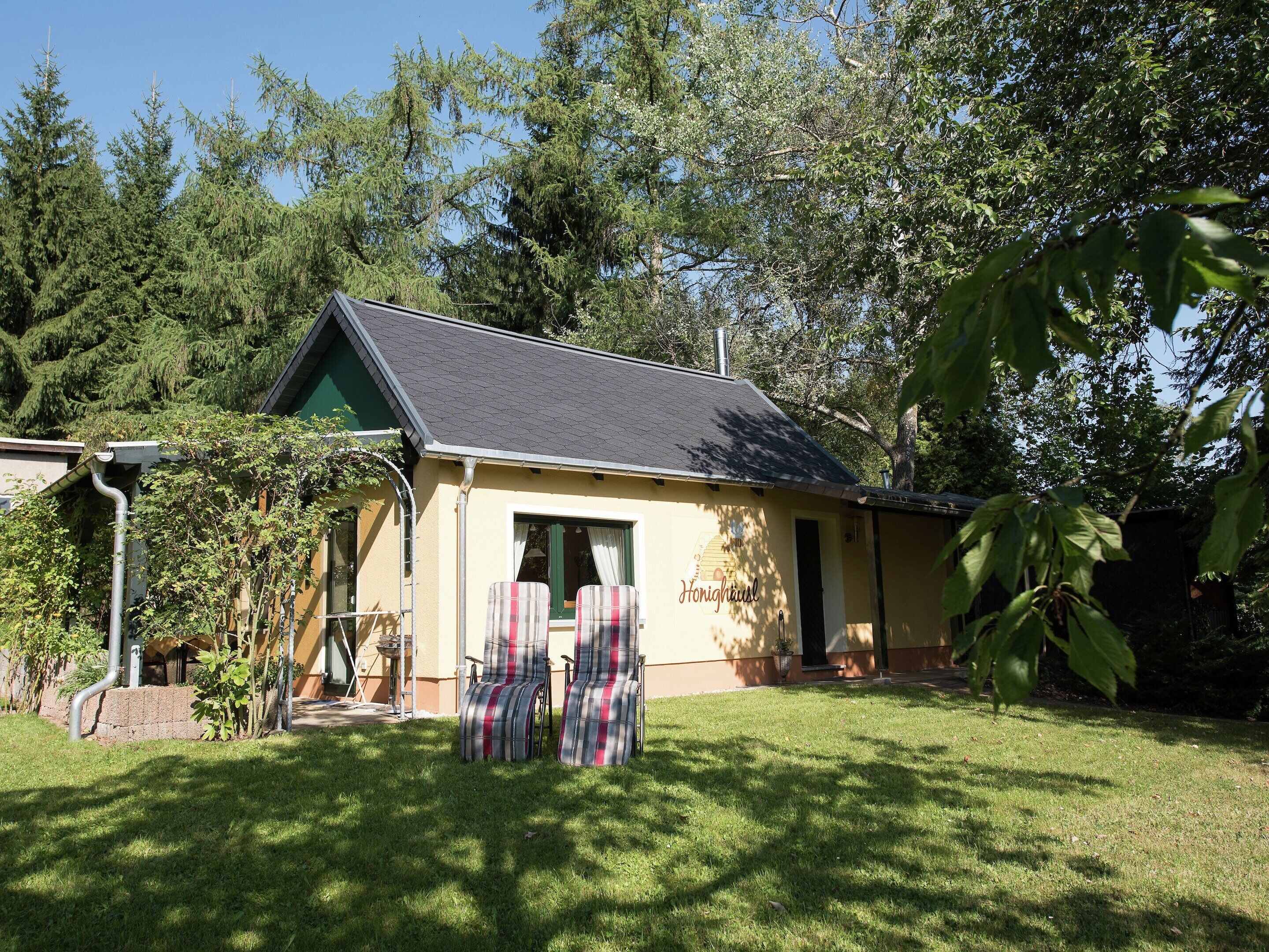 A small house with a sloped roof and a front door. There are two plaid chairs outside.