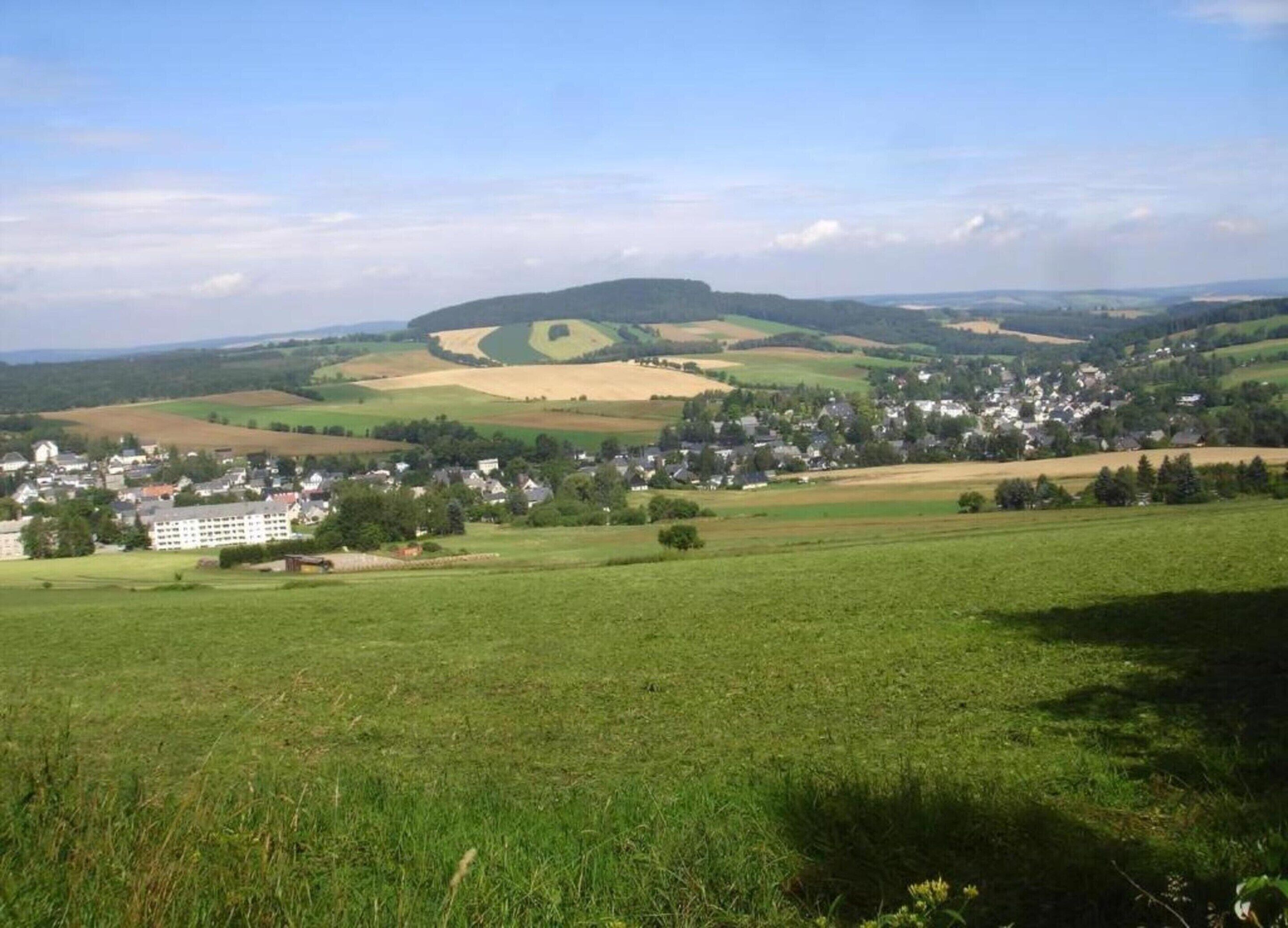 A rural landscape with a village, green fields, and a hill in the background.
