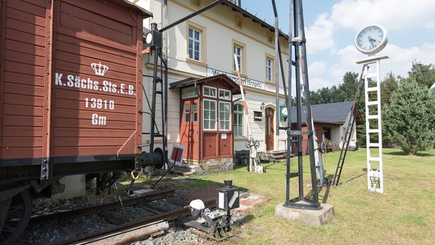 A vintage train station with a clock tower, a building labeled "K. Sächs. St. E. B. 13910", and a small outdoor seating area. - Apartment in Saxony With Terrace (Crottendorf)