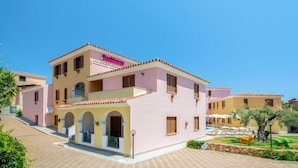 A pink building with a sign reading "Residence." It features a tiled roof, multiple windows, and a small balcony.