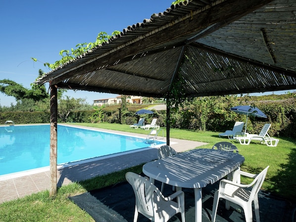 A pool area with a covered seating area, lounge chairs, and a table.