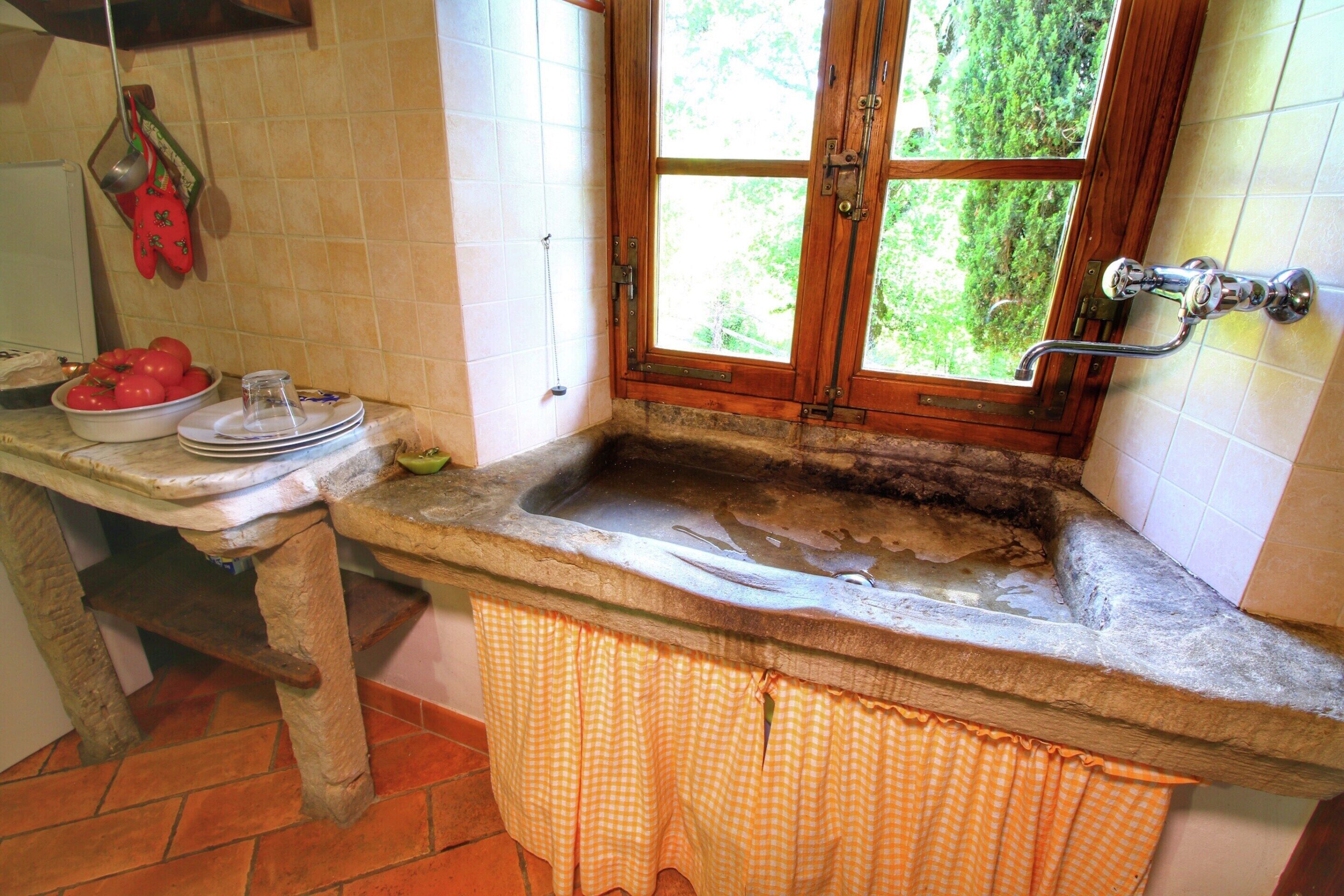 A kitchen with a stone countertop, a window with a view of greenery, and a sink with a metal faucet.