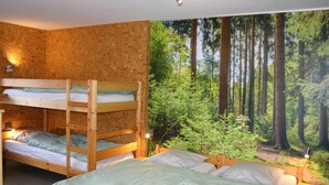 Een kamer met stapelbedden, een groot bosdecor en een plafondlamp.