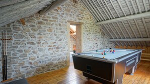 Een gezellige kamer met een pooltafel, stenen muren, houten vloeren en een schuine plafond.