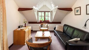 A cozy attic room with a sloped ceiling, a wooden desk, a black leather sofa, and a dining table. - Peaceful Nature Stay in Bohon (Durbuy)