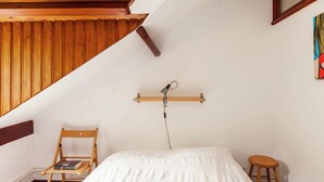A small, cozy room with a sloped ceiling, a wooden chair, a small stool, and a bed with a white quilt. - Peaceful Nature Stay in Bohon (Durbuy)