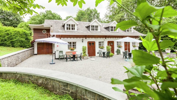 A two-story building with a gravel courtyard, outdoor seating, and a stone retaining wall. - Peaceful Nature Stay in Bohon (Durbuy)